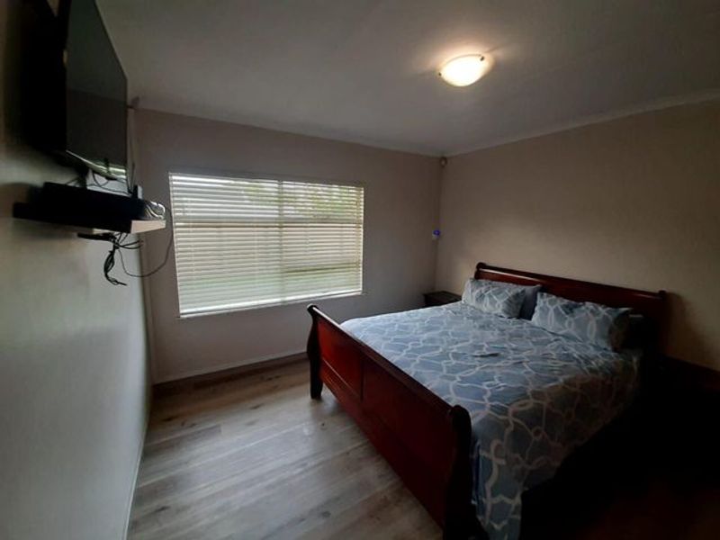 A bedroom featuring light-toned wood-look flooring, a window with fitted blinds, and a ceiling-mounted light fixture.