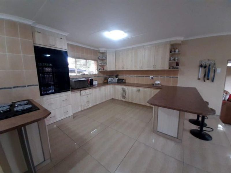A spacious kitchen featuring light-toned cabinetry, a breakfast bar, tiled flooring, and integrated cooking appliances.