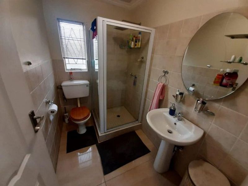 A functional bathroom featuring a corner shower enclosure, pedestal basin, and toilet, finished with neutral wall and floor tiling.