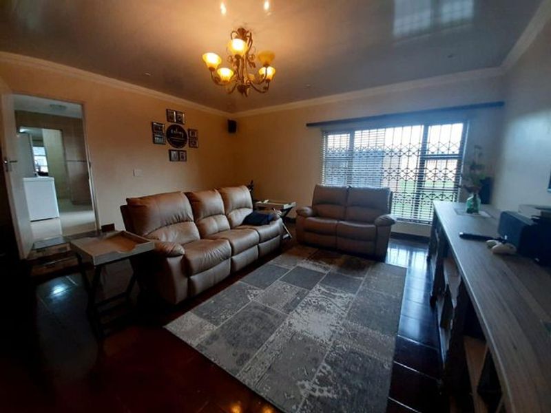 A comfortable living room featuring tiled flooring, a decorative chandelier, and a large window fitted with security bars.
