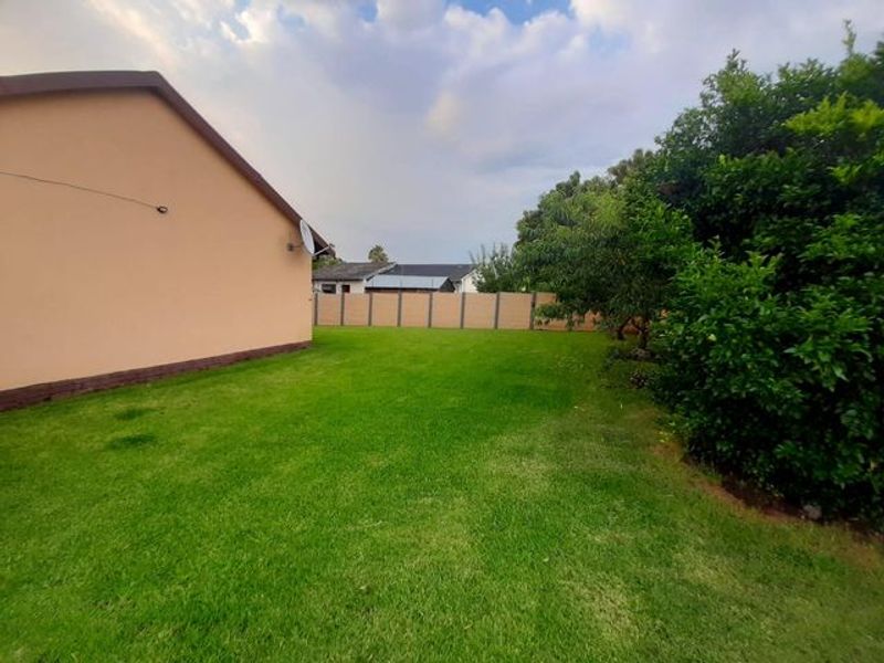 A spacious rear garden featuring a well-maintained lawn, perimeter boundary wall, and established greenery, providing a private outdoor space.