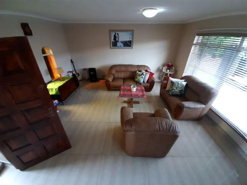 A spacious living room featuring large format floor tiles, neutral wall tones, and horizontal window blinds, providing a comfortable and functional family living space.