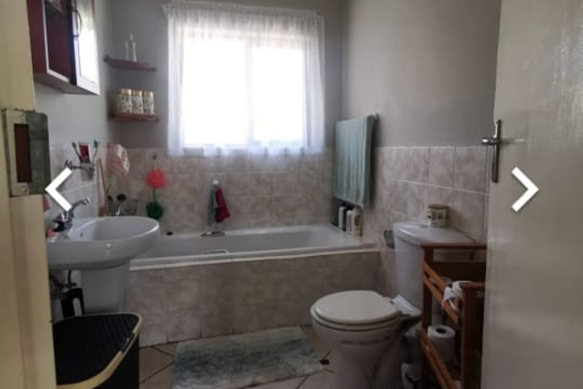 A functional bathroom featuring a pedestal basin, built-in bathtub, and neutral ceramic tiling throughout.
