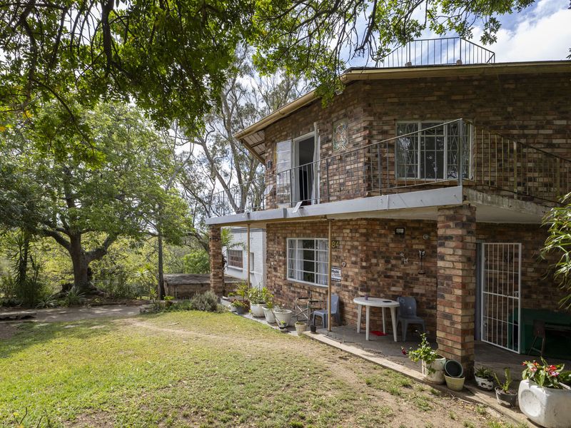 Rear view of a two-story brick house featuring a covered patio, an upper-level balcony with metal railings, and a roof terrace area.