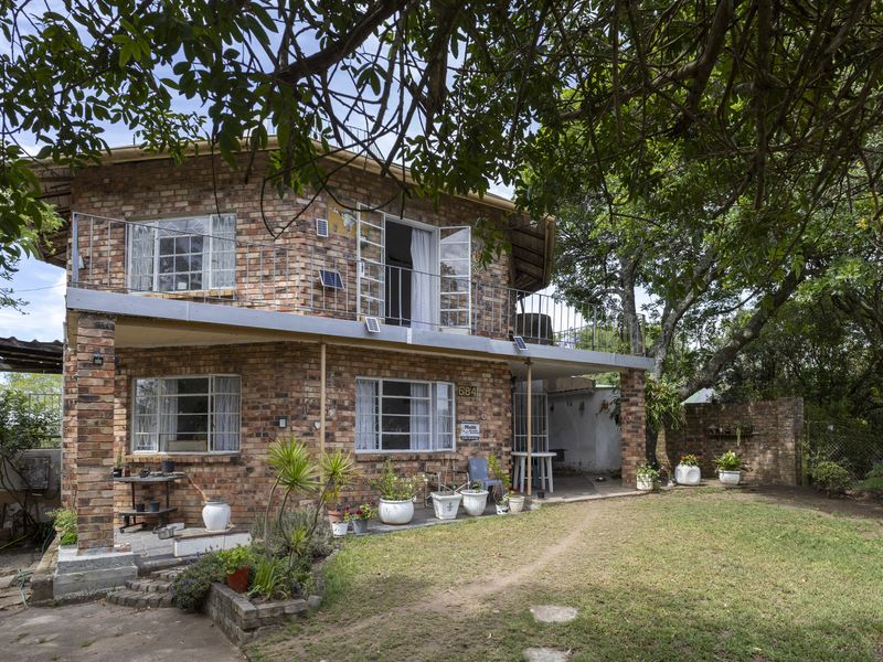 Two-story face brick house featuring an upper-level balcony, covered ground-floor patio, and established garden surroundings.