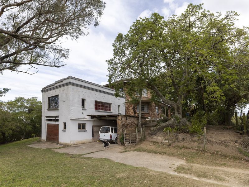 Exterior view of a multi-level house featuring a brick facade, attached garage, and carport, set within a large, mature garden area.