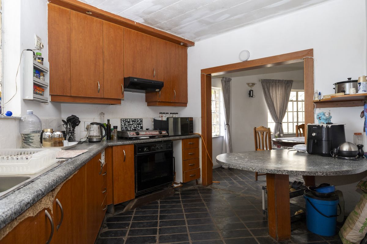 A dated kitchen featuring wood-tone cabinetry, stone-look countertops, and dark floor tiles, with an open-plan layout leading into the adjacent dining area.
