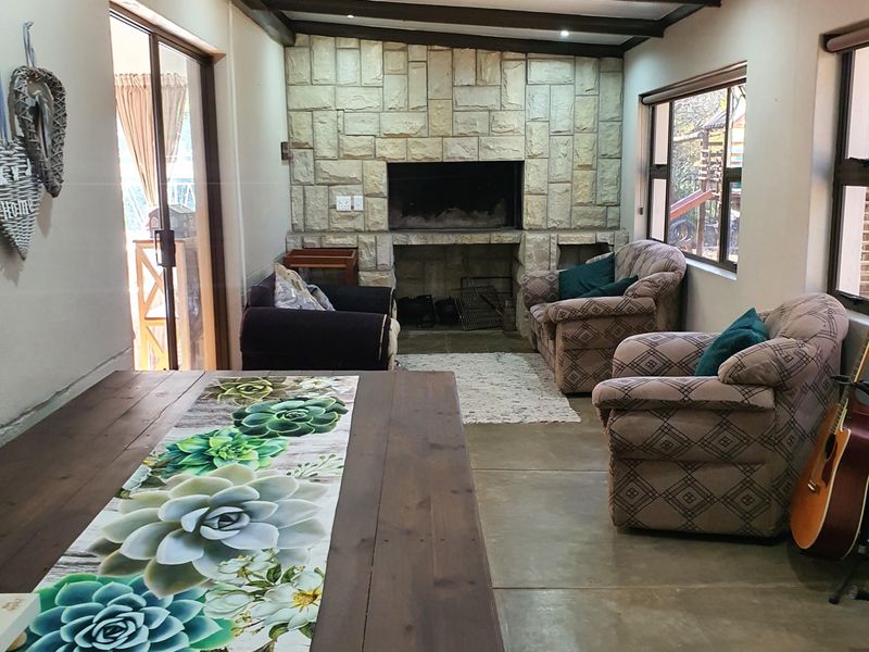 Spacious living area featuring a prominent stone fireplace, exposed timber ceiling beams, and concrete flooring with direct access to the outdoor patio.