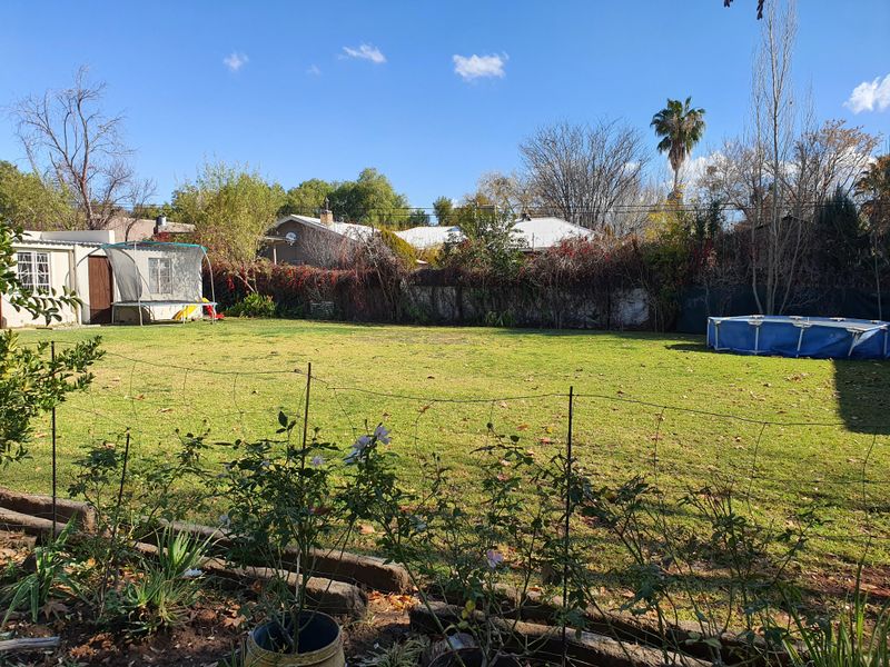 A spacious, level backyard featuring a large lawn area, perimeter fencing, and established garden borders.