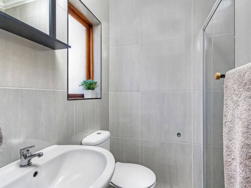A modern, well-maintained bathroom featuring floor-to-ceiling grey ceramic tiling, a pedestal washbasin, a toilet, and a glass-enclosed shower.