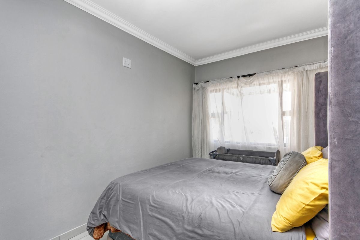 A well-lit bedroom featuring neutral grey walls, crown molding, and a large window with sheer curtains.