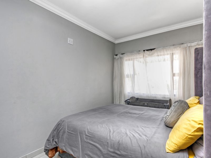 A well-lit bedroom featuring neutral grey walls, crown molding, and a large window with sheer curtains.
