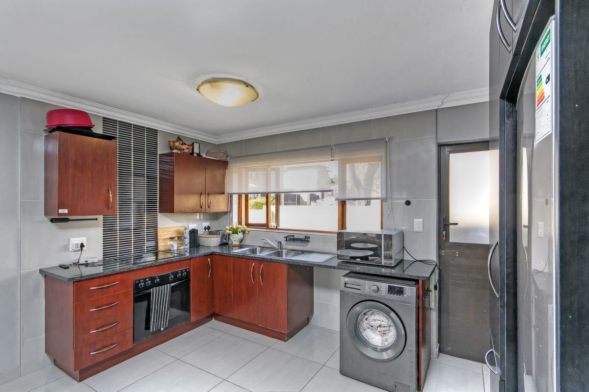 A functional kitchen featuring dark wood cabinetry, granite countertops, a double basin sink, built-in oven, and tiled finishes throughout.