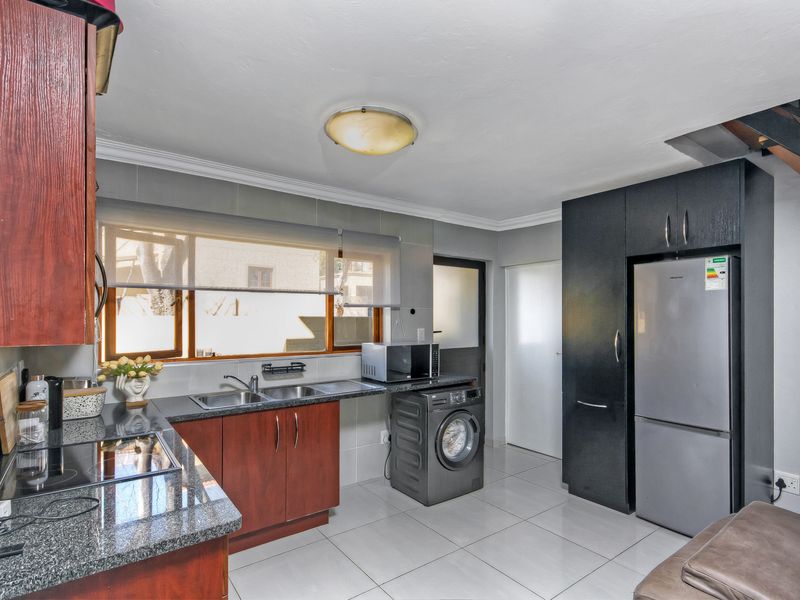 Functional kitchen featuring granite countertops, double basin sink, electric hob, and ample built-in cabinetry with tiled flooring.