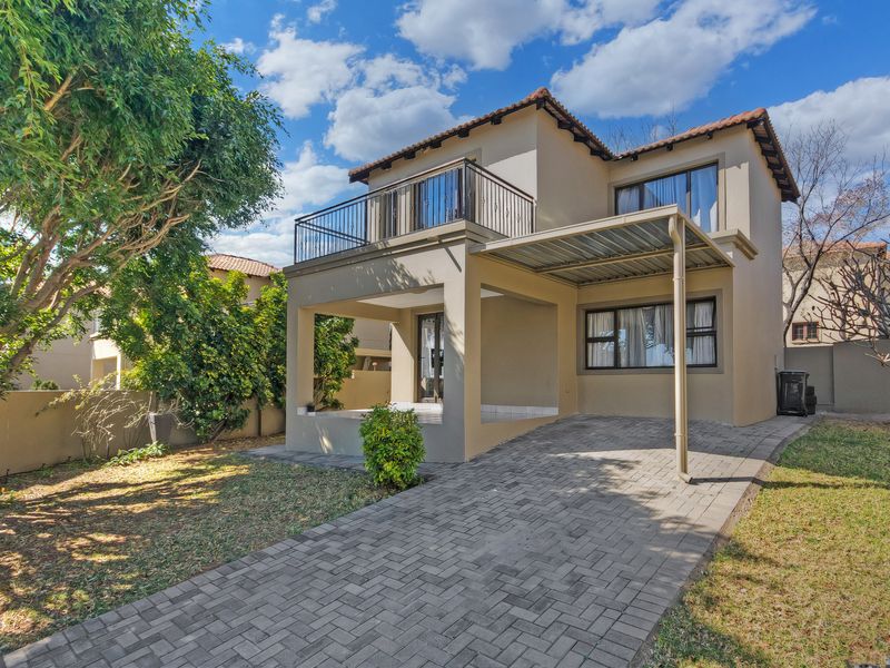Rear view of a double-story townhouse featuring a paved driveway, covered patio area, and an upper-level balcony with wrought iron railings.