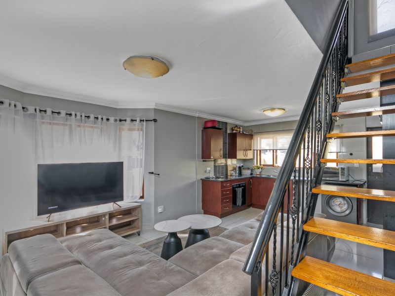 Open-plan living area featuring a compact kitchen with built-in cabinetry and a staircase leading to the upper level.