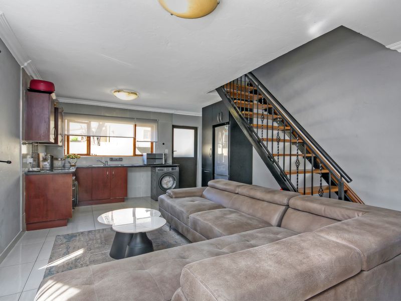Open-plan living area featuring a compact kitchen with built-in cabinetry, tiled flooring, and a staircase leading to the upper level.