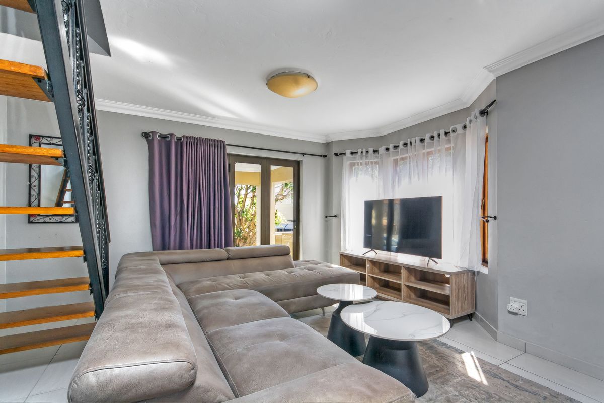 A bright living room featuring tiled flooring, cove cornicing, and a staircase, with direct access to the outdoor area through french doors.