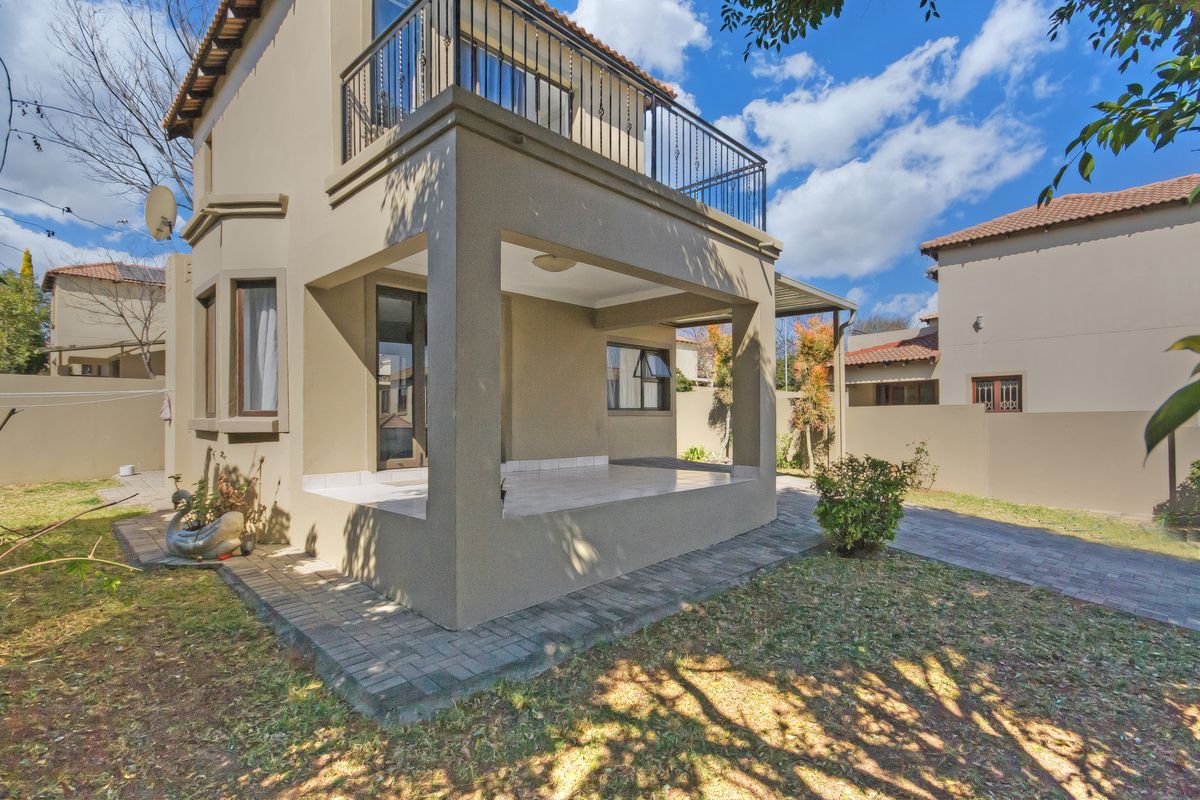 Rear view of the townhouse featuring a covered tiled patio, an upper-level balcony with metal railings, and a paved garden area.