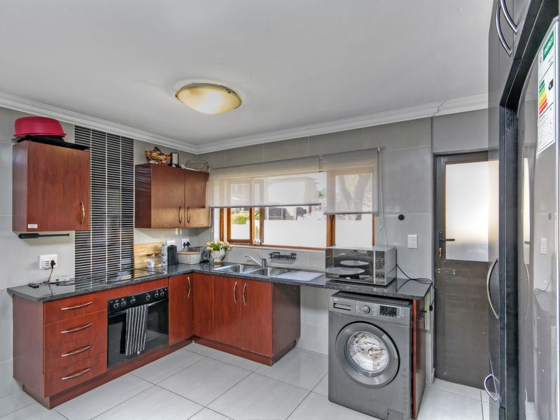 A functional kitchen featuring dark wood cabinetry, granite countertops, a double basin sink, built-in oven, and tiled finishes throughout.