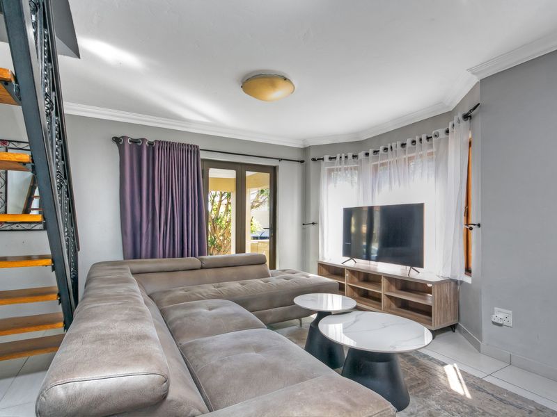 A bright living room featuring tiled flooring, cove cornicing, and a staircase, with direct access to the outdoor area through french doors.