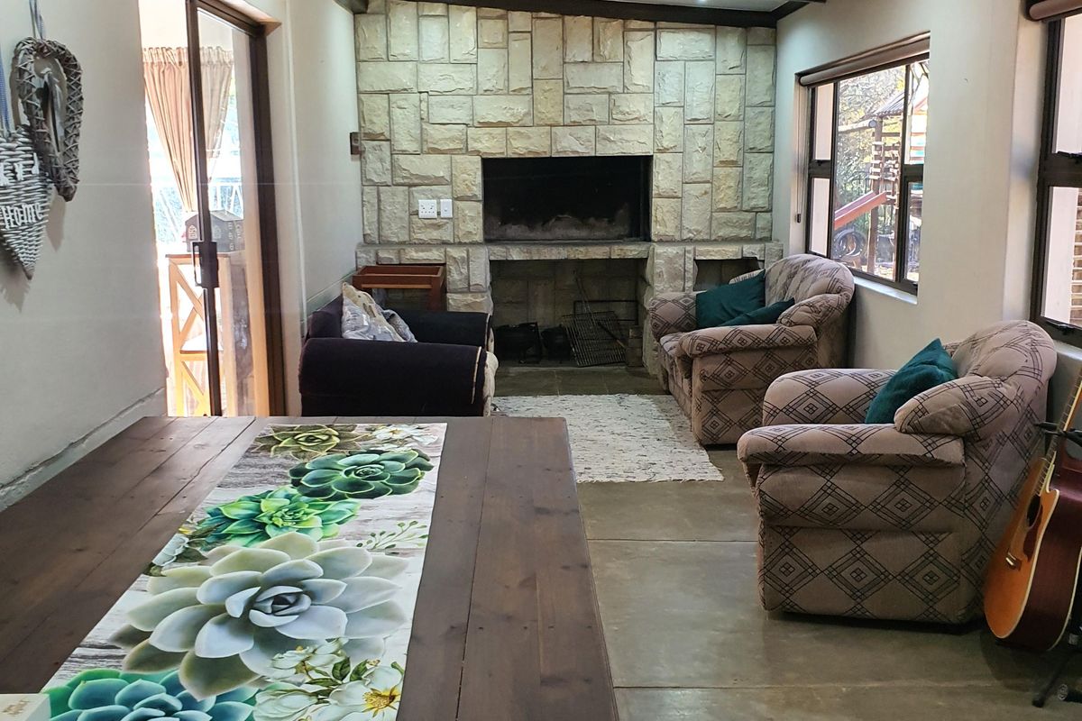 Spacious living area featuring a prominent stone fireplace, exposed timber ceiling beams, and concrete flooring with direct access to the outdoor patio.