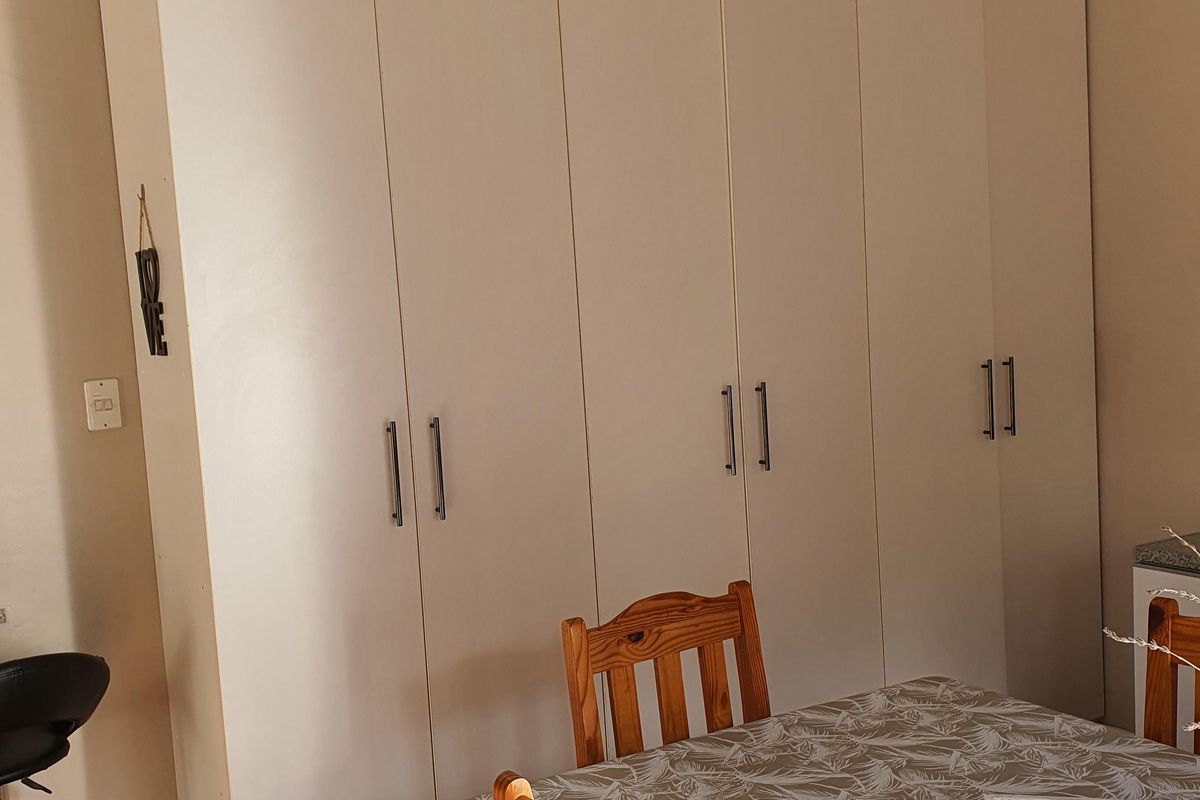 A bedroom featuring floor-to-ceiling built-in cupboards and warm hardwood flooring, providing ample storage space.