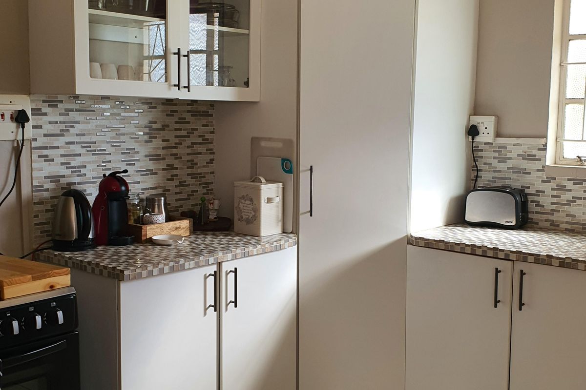 A functional kitchen featuring white built-in cabinetry, a mosaic tiled backsplash, and light-colored floor tiles, providing a clean and organized workspace.