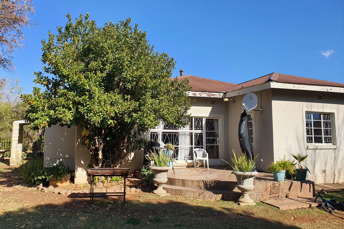 Rear view of the house featuring a tiled patio area, security gates, and a mature garden setting.