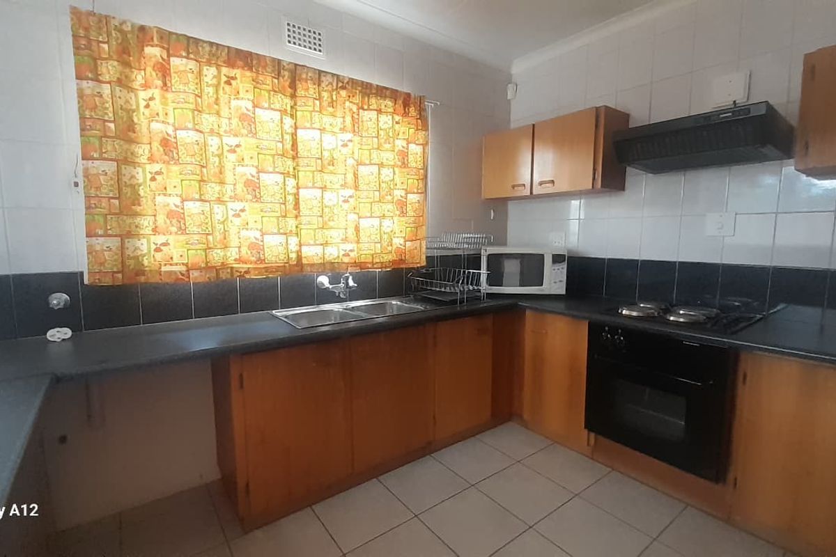 Functional kitchen featuring wooden cabinetry, dark laminate countertops, built-in oven, hob, and extractor fan with tiled splashbacks and flooring.