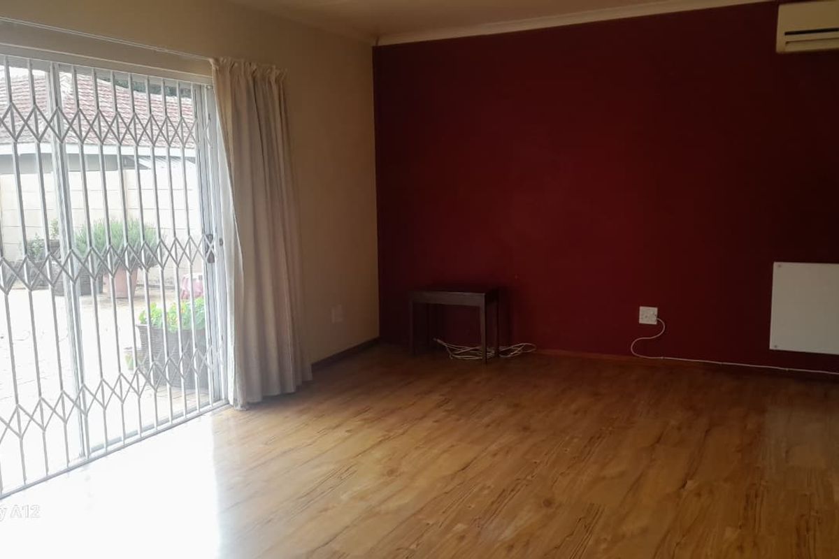 Spacious living area featuring laminate flooring, a wall-mounted air conditioner, and a sliding glass door with a security gate leading to the patio.