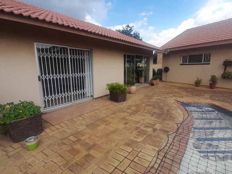 Rear exterior view featuring a paved patio area, swimming pool, and access to the home via sliding doors with security gates.