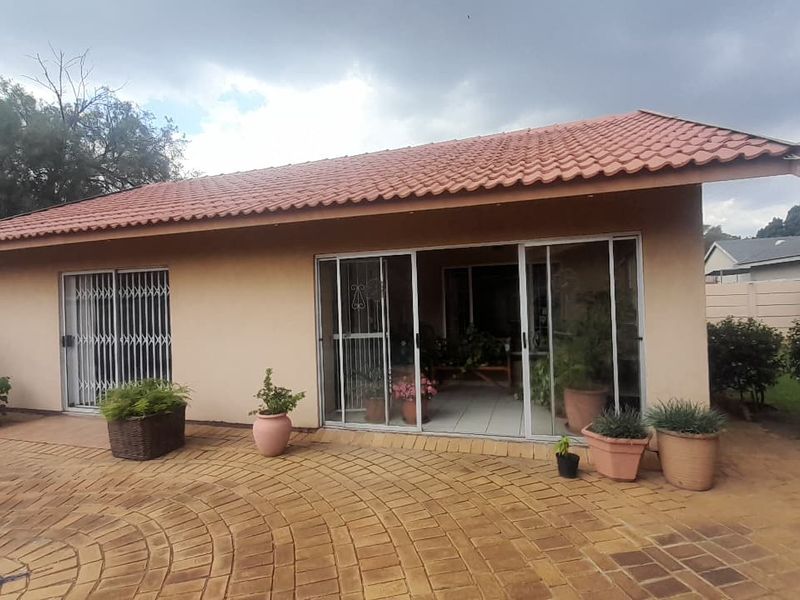 Rear view of the house featuring a paved patio area, terracotta tiled roof, and sliding glass doors with security gates.