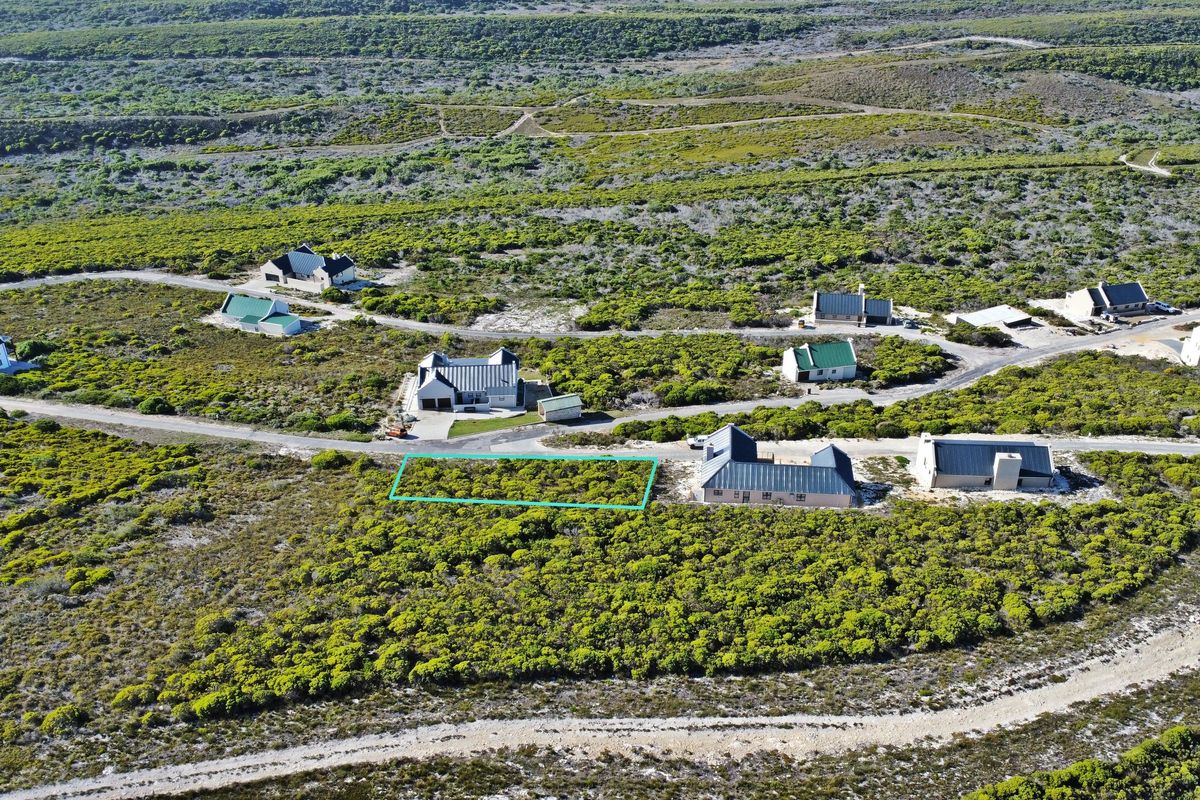 Aerial view of a vacant residential plot situated within a coastal estate, featuring natural vegetation and access to a paved road.