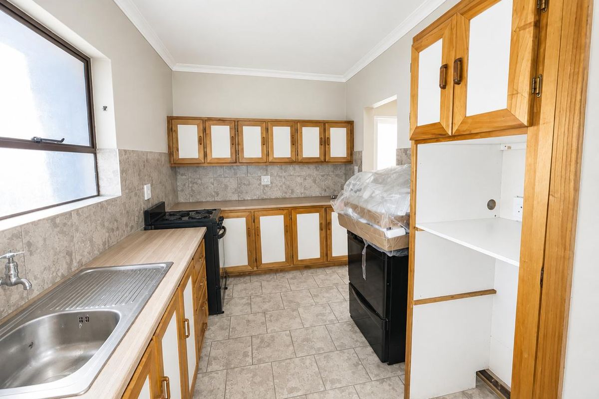 A functional kitchen featuring wooden cabinetry, laminate countertops, a stainless steel sink, and tiled backsplash, offering a practical layout for daily use.