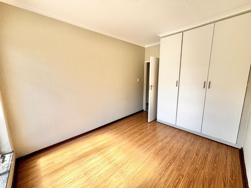 A bright, empty bedroom featuring light-toned laminate flooring and ample built-in cupboard storage space.