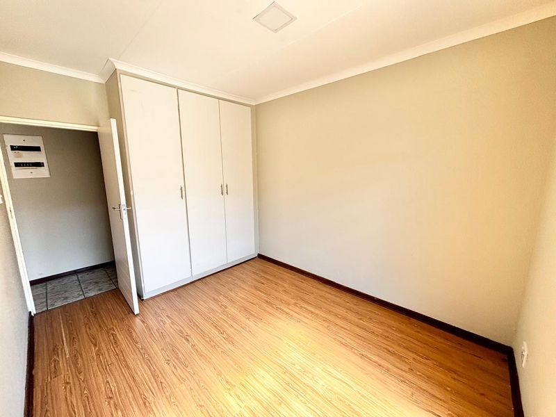 A clean, empty bedroom featuring neutral walls, laminate flooring, and built-in cupboards, providing a versatile space ready for personalization.