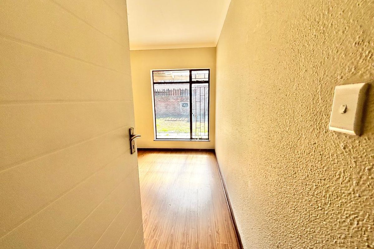 A vacant bedroom featuring laminate flooring, a window with security bars, and a neutral wall finish, ready for personalization.