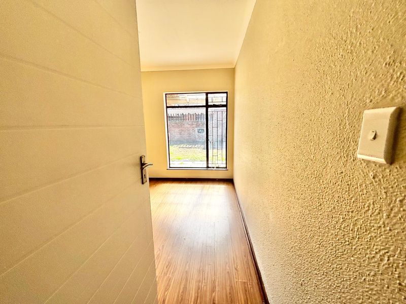 A vacant bedroom featuring laminate flooring, a window with security bars, and a neutral wall finish, ready for personalization.