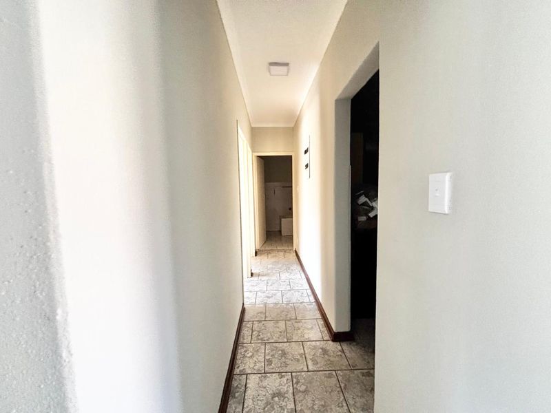 A clean, neutral-toned hallway featuring tiled flooring and simple light fixtures, providing access to multiple rooms within the townhouse.