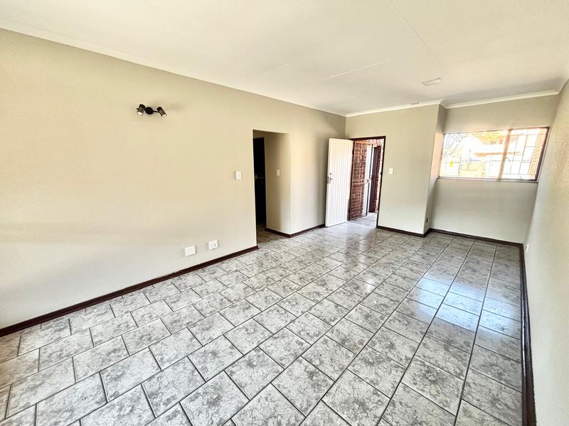A spacious, empty living area featuring neutral wall tones, tiled flooring, and a security gate leading to the exterior.