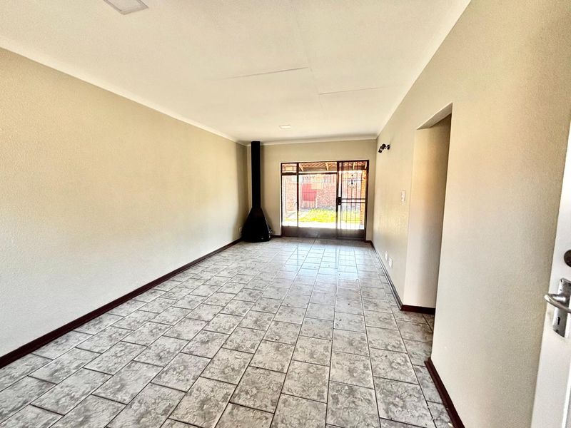 Spacious living area featuring neutral walls, tiled flooring, and a freestanding fireplace, with direct access to the rear garden through a security sliding door.