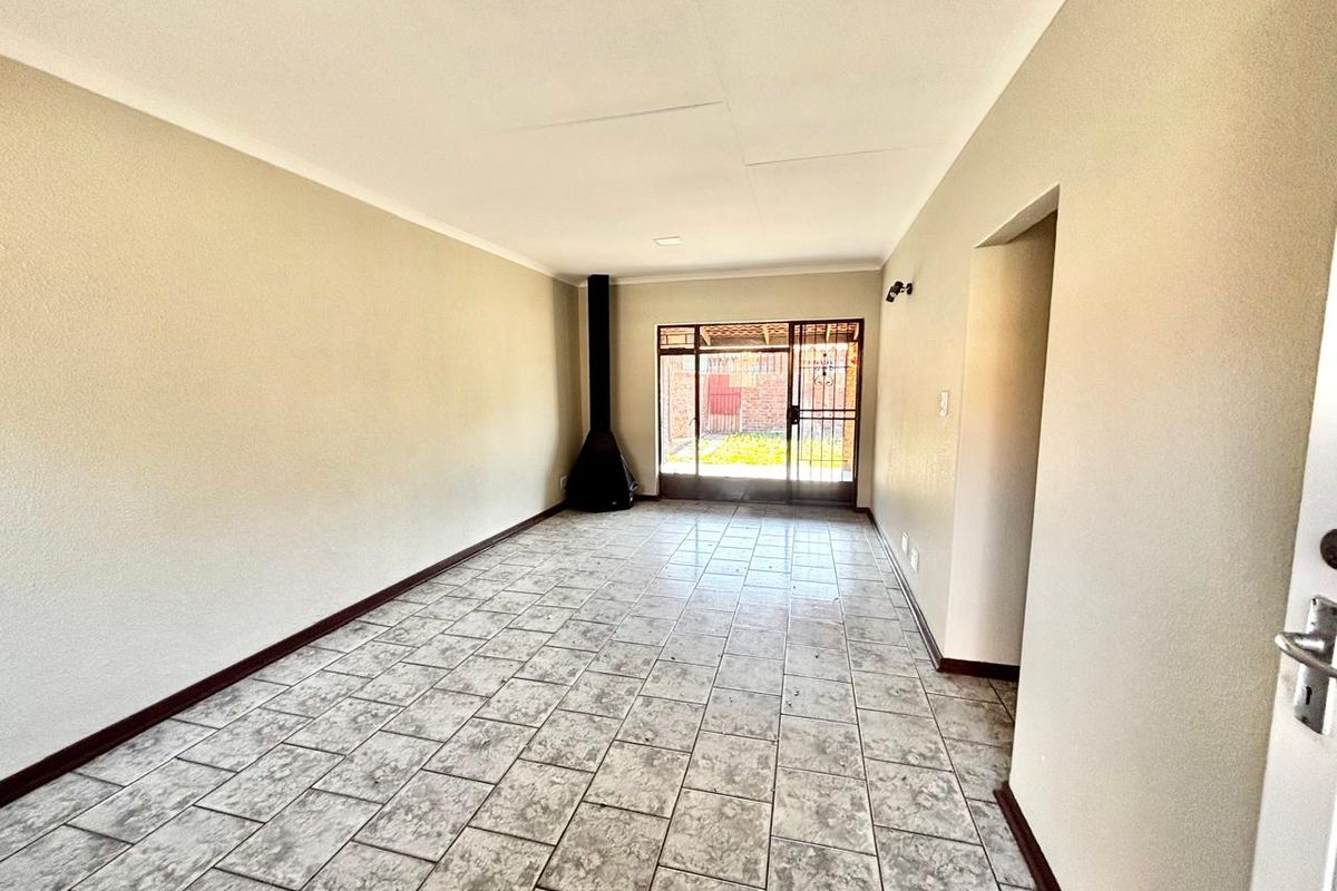 Spacious living area featuring neutral walls, tiled flooring, and a freestanding fireplace, with direct access to the rear garden through a security sliding door.