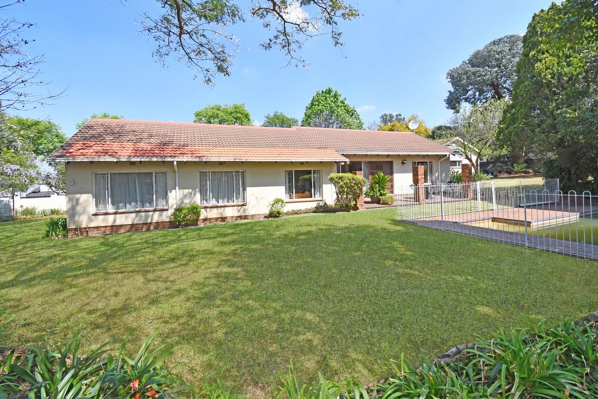 Rear view of the house featuring a spacious lawn, a swimming pool with safety fencing, and a paved patio area.