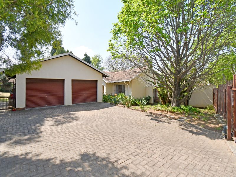 Front view of the property featuring a double garage, paved driveway, and established garden with mature trees and secure perimeter fencing.
