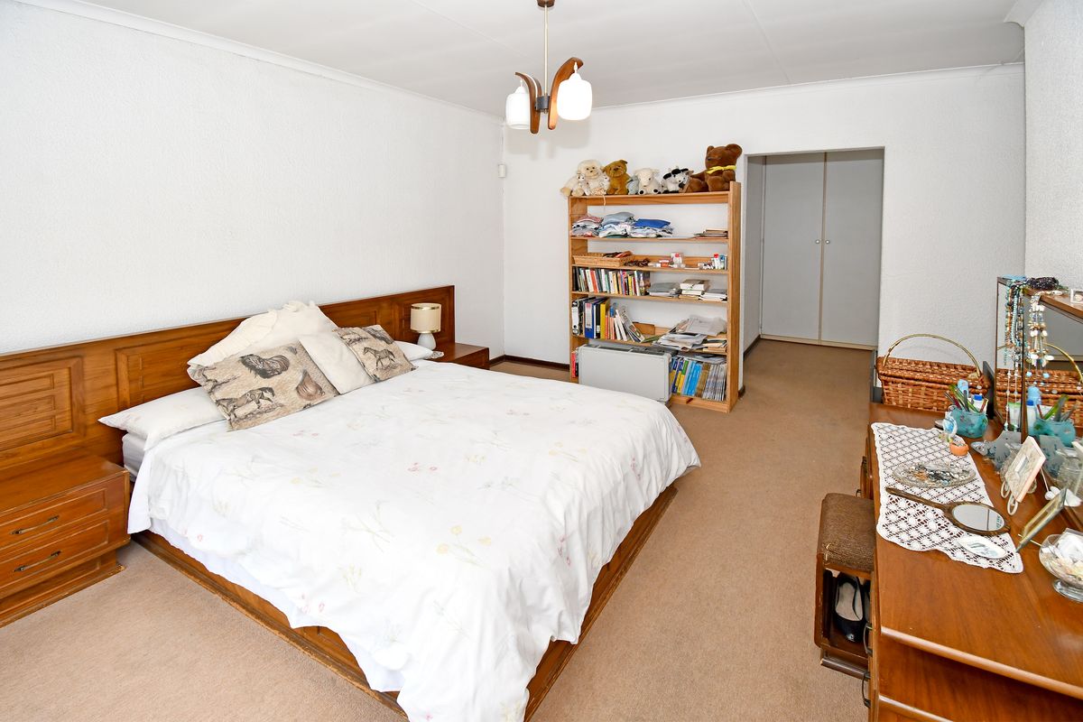 A spacious bedroom featuring neutral carpeting, built-in cupboards, and a central ceiling light fixture, offering a functional and well-maintained living space.