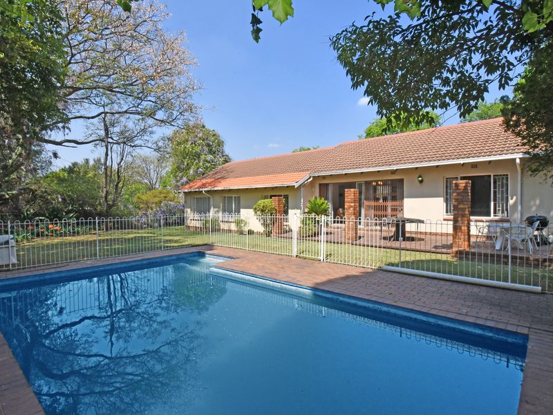 A well-maintained backyard featuring a swimming pool with brick paving, a metal safety fence, and a covered patio area attached to the main house.