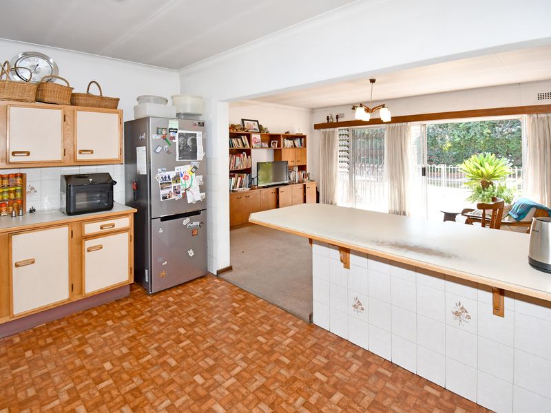 Open-plan kitchen and living area featuring dated cabinetry, tiled breakfast bar, and direct access to the outdoor patio through sliding glass doors.