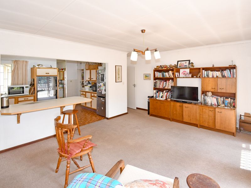 Open plan living and kitchen area featuring a breakfast bar, built-in cabinetry, and carpeted flooring, offering a functional layout with potential for modernization.