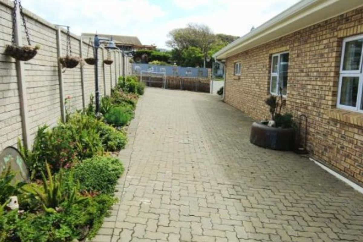 A side pathway featuring brick paving, a face brick exterior wall, and a landscaped garden bed along the boundary wall.